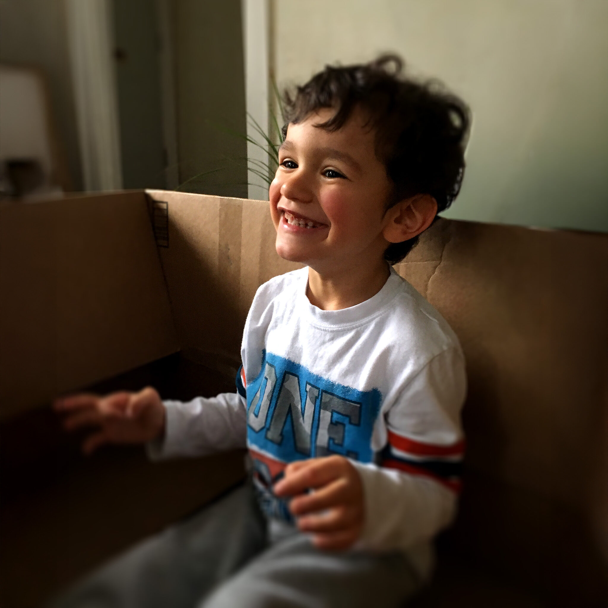Anthony smiles brightly while sitting in a cardboard box, a joyful image representing hope for Fragile X syndrome.